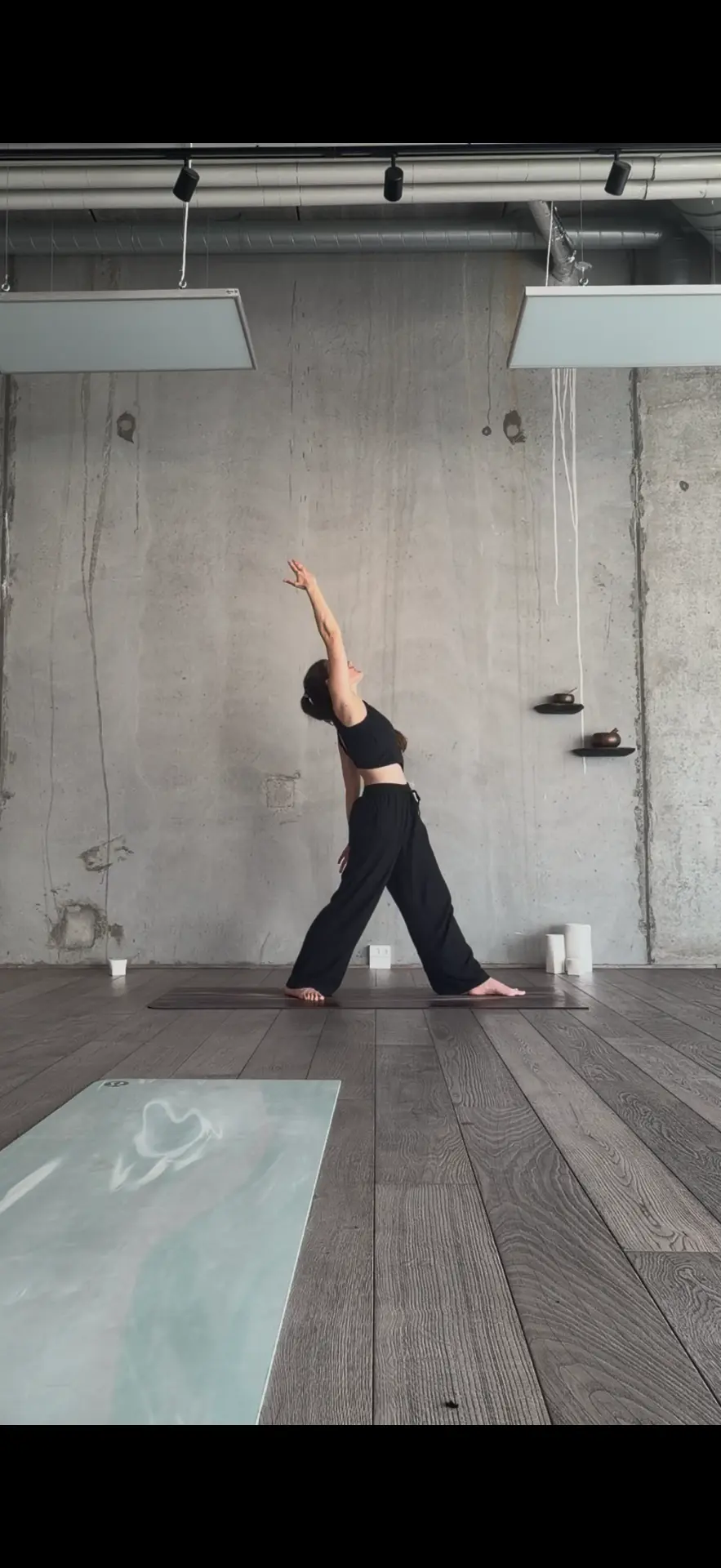 Chiara practicing a crescent lunge with arms lifted in a concrete studio